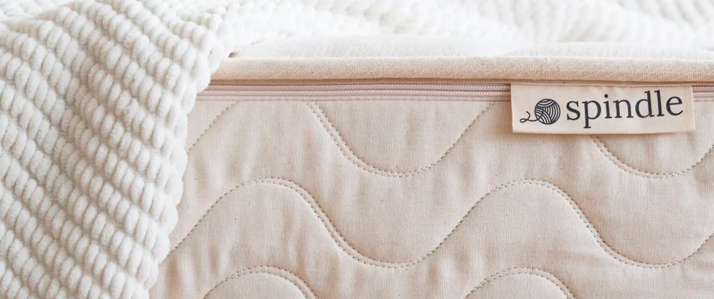 Close-up view of the side of a Spindle 10in organic mattress with a white blanket hanging over the side