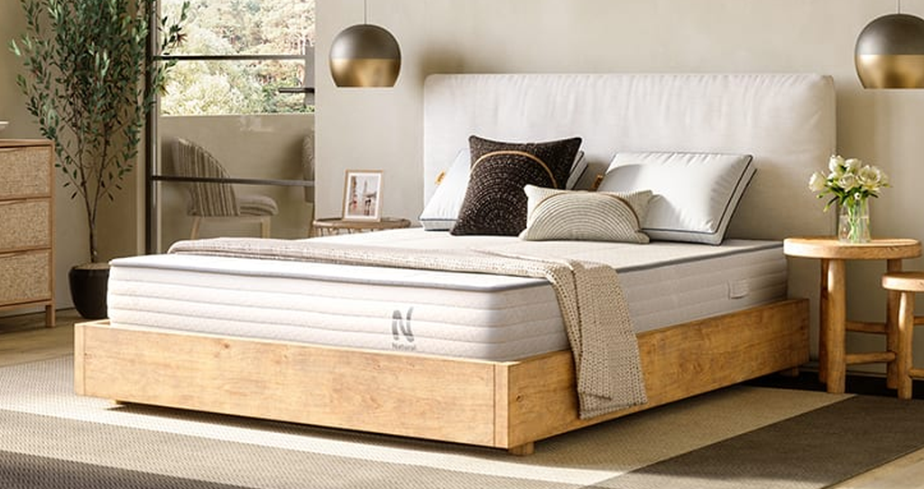 Light grey colored Nolah Natural mattress in a wooden frame with a blanket and four pillows