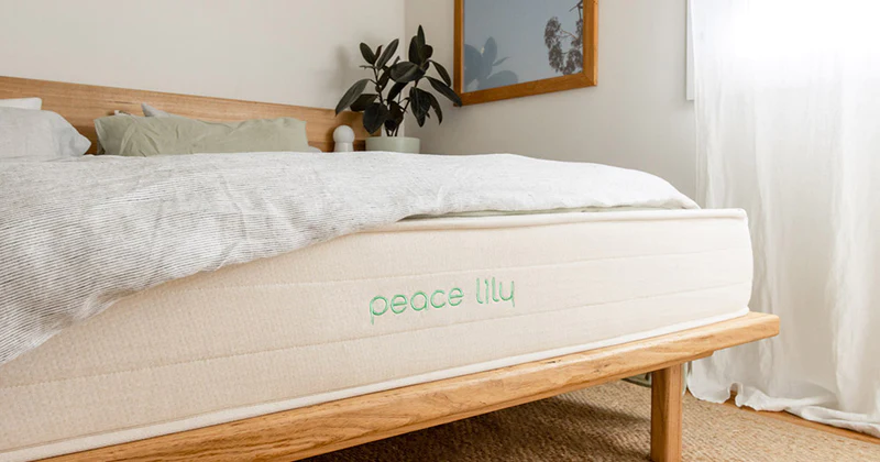 Close-up view of the bottom edge of a mattress with the blanket pulled up to show Peace Lily logo