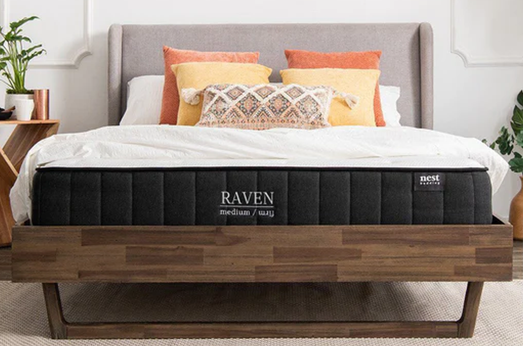 Black colored Nest Bedding Raven mattress with seven pillows on dark brown wooden frame